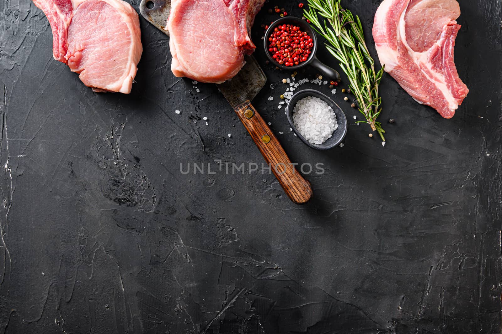 Organic Pork meat chop set over american classic butcher knife or cleaver with spices and rosemary and red pepper on black slate table top view. Space for text in bottom side by Ilianesolenyi