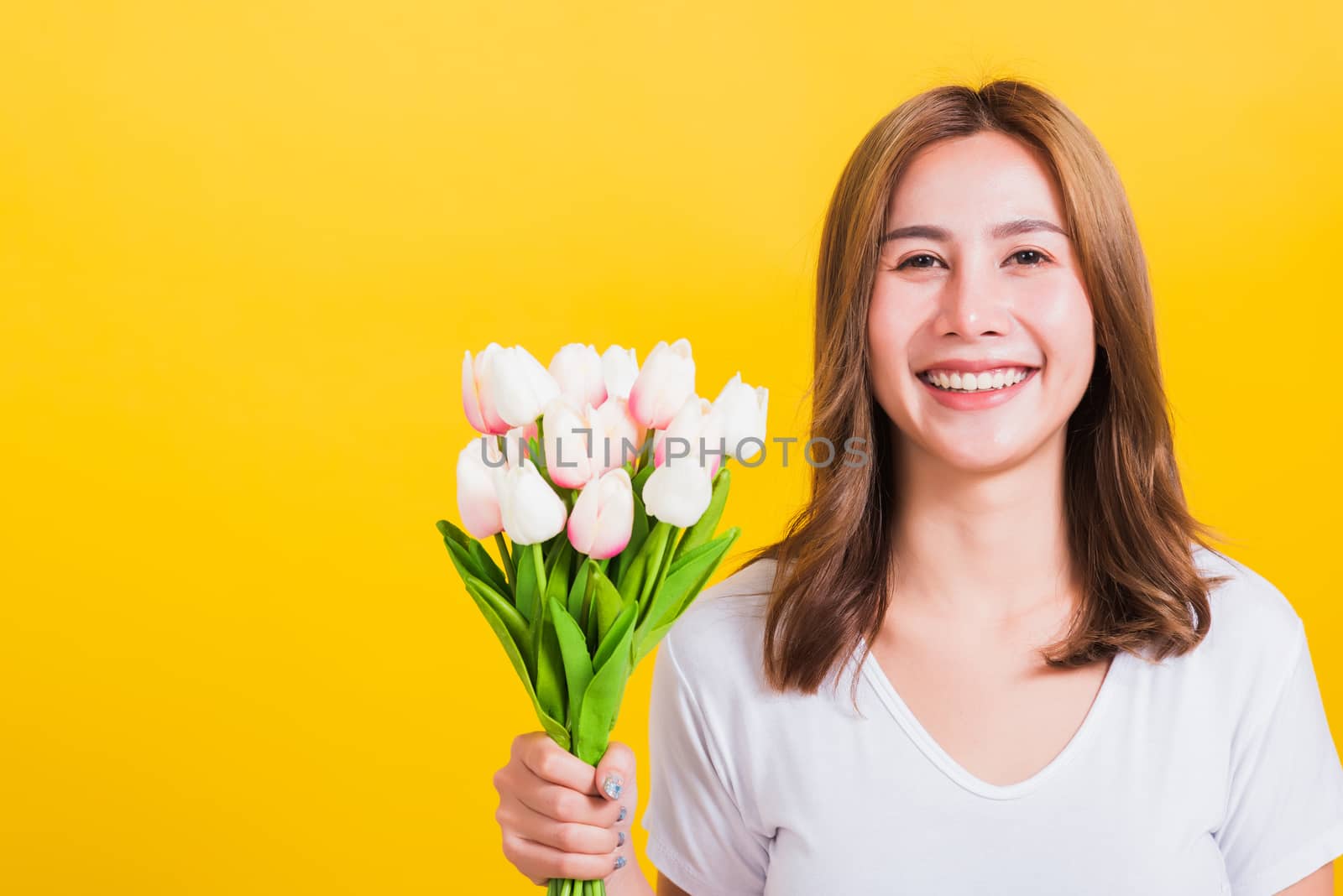 Portrait Asian Thai beautiful happy young woman smiling, screaming excited hold flowers tulips bouquet in hands and looking to camera, studio shot isolated on yellow background, with copy space