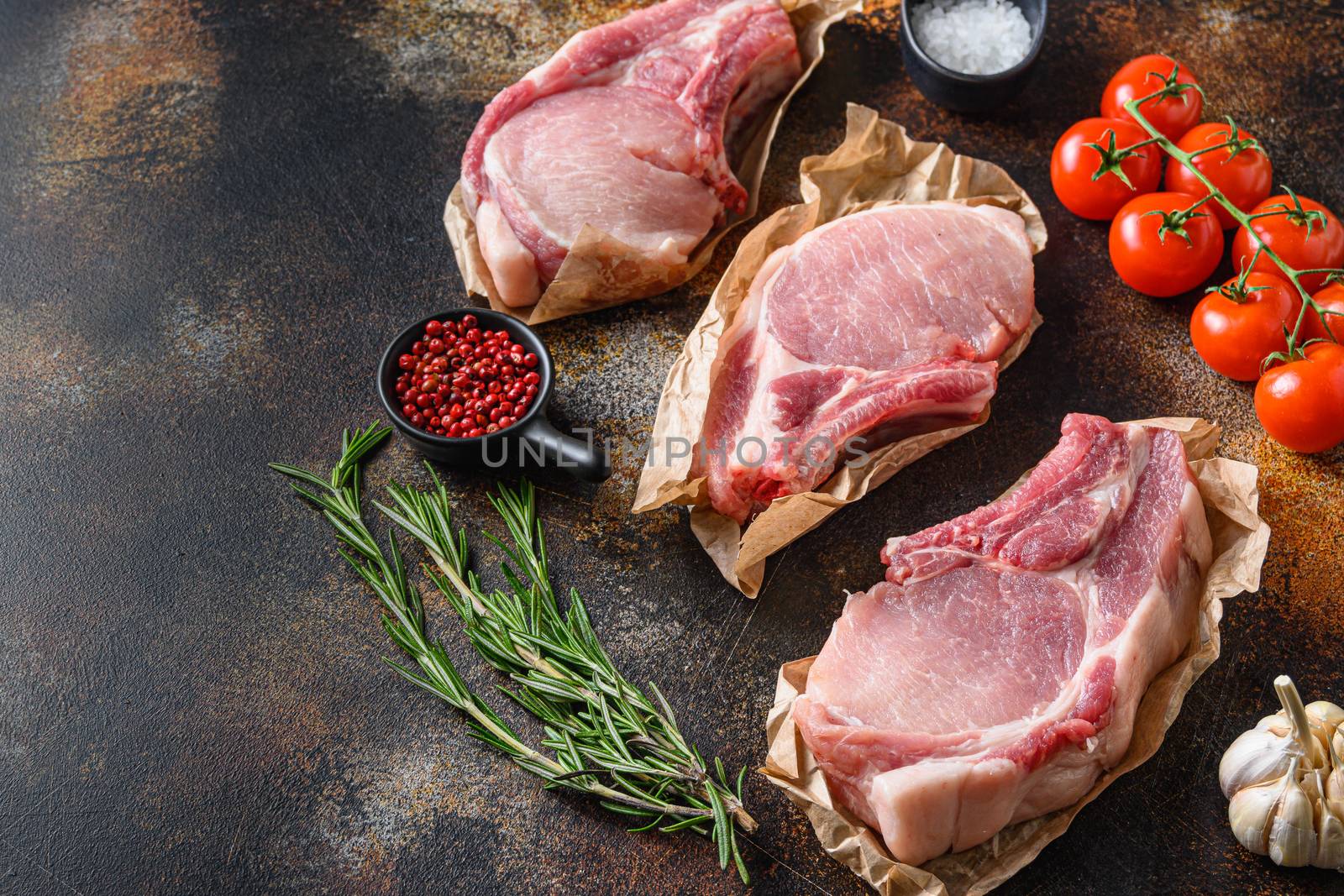 Tree bunch raw pork chops arranged with herbs, oil and spices. Cooking meat. On dark background with space for text.