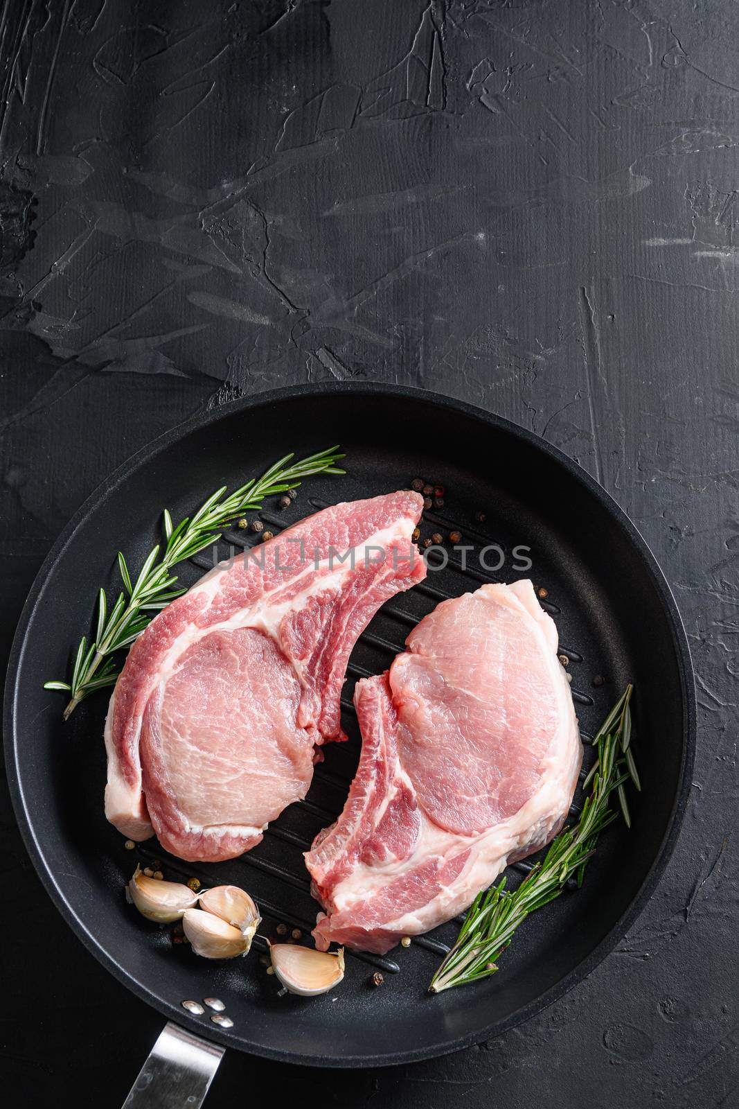 pork rib chops in frying pan grill skillet with herbs, spices top view black stone bakground space for text vertical by Ilianesolenyi