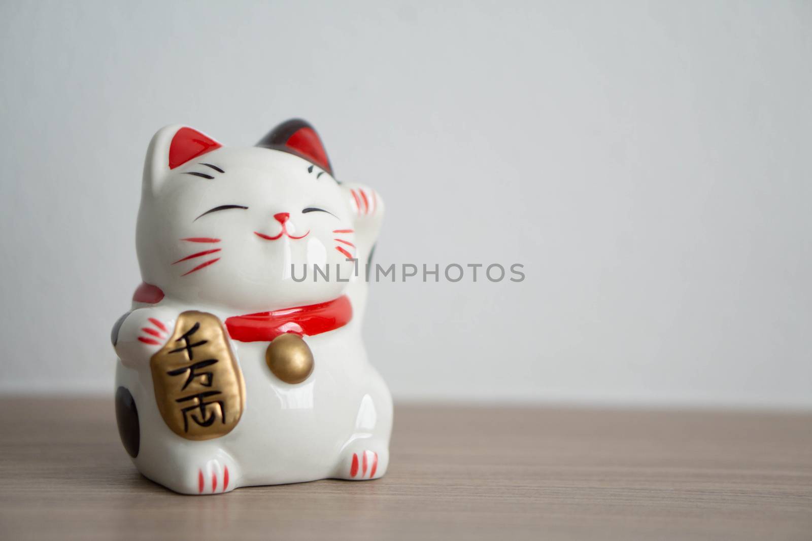 Maneki neko lucky cat show text on hand meaning rich on wood table background, select focus