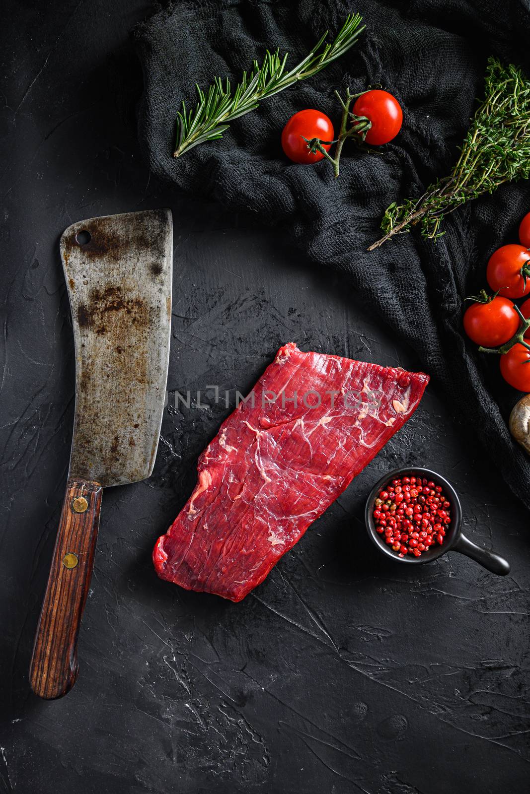Raw, flap or flank, also known Bavette steak near butcher knife with pink pepper and rosemary. Black background. Top view vertical by Ilianesolenyi