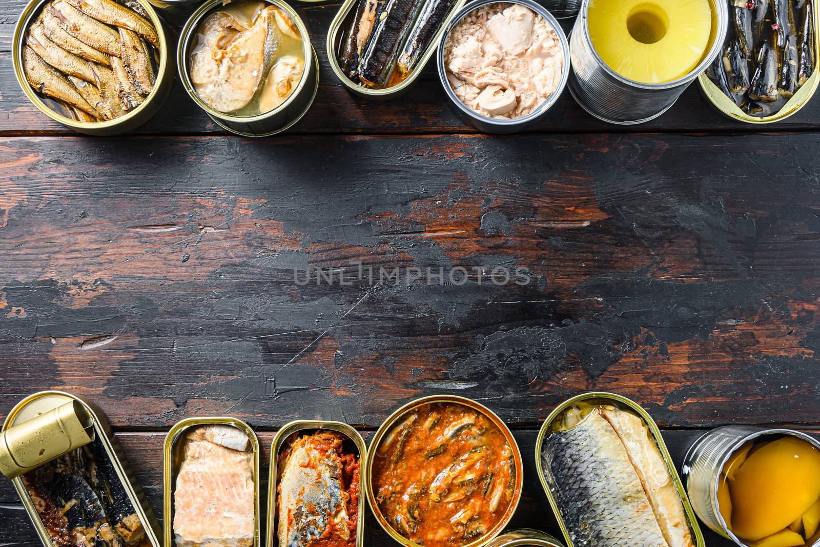 Copyspace concept for text between two lines of Various canned prepared vegetables, meat, fish and fruits in tin cans. On a wooden background top view.