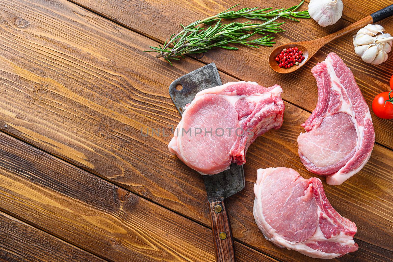 Raw pork meat chopes with herbs and spices with meat american cleaver on wooden background side view space for text. Diagonal.