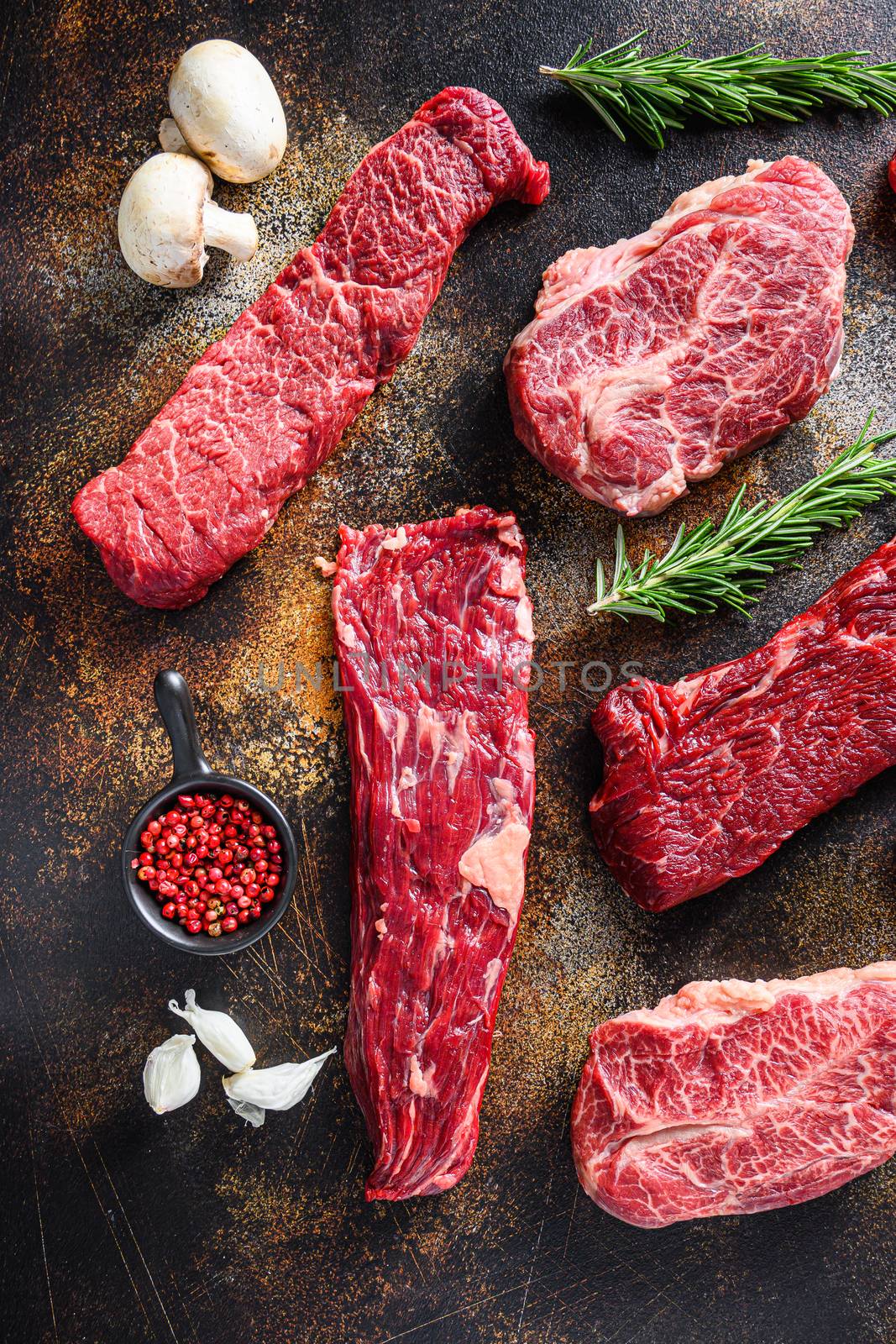 Organic set of raw alternative beef steaks flap flank Steak, machete steak or skirt cut, Top blade or flat iron beef and tri tip, triangle roast with denver cut side view over old rustic metal surface close up.