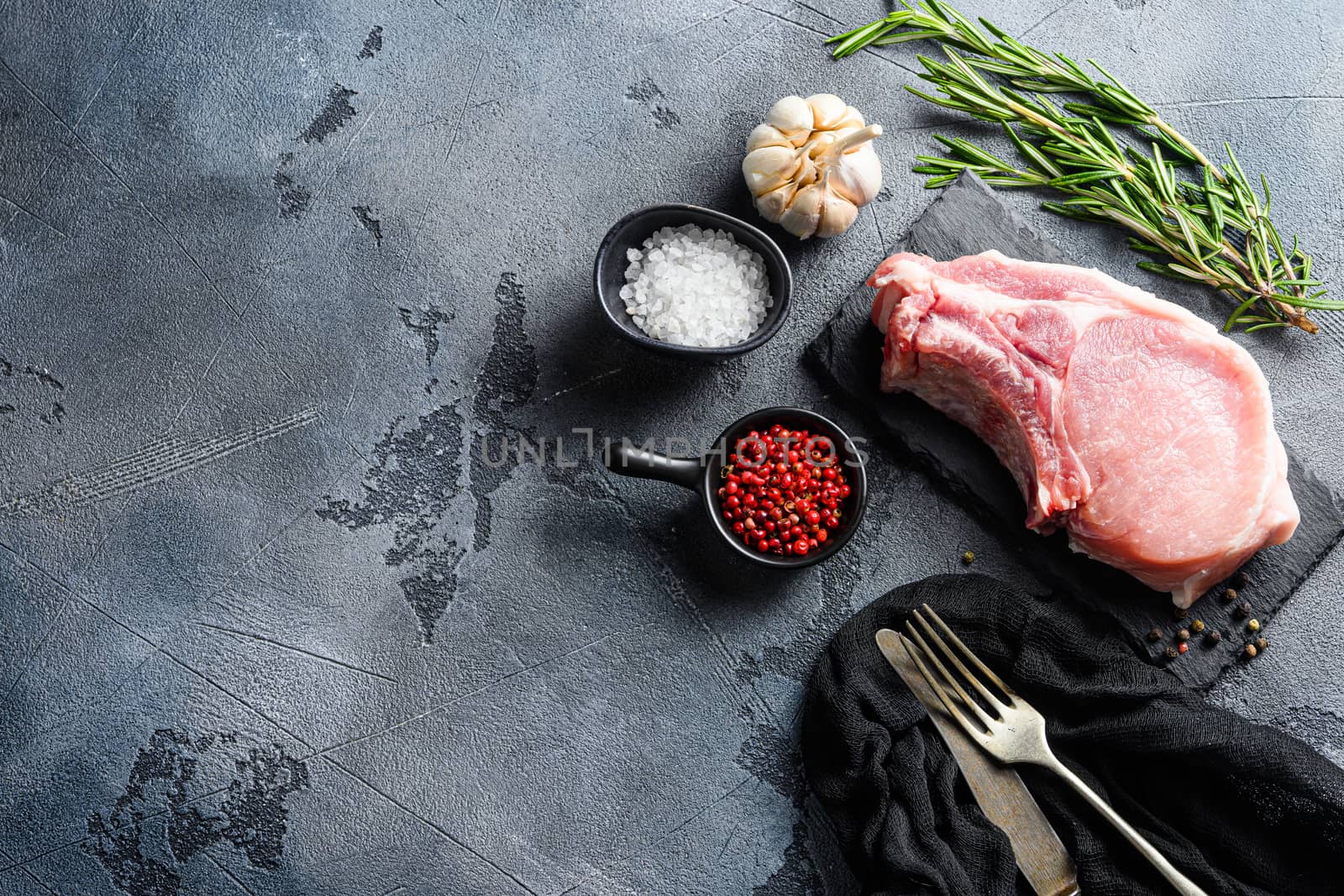 Pork chopes with herbs, spices on black slate over grey background top view. space for text.