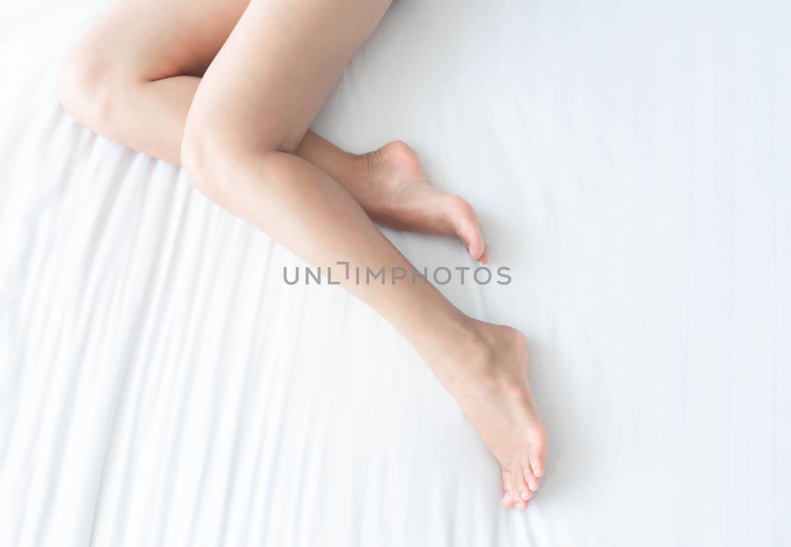 Closeup woman legs on white bed with over light form window, beauty and skin care concept, selective focus