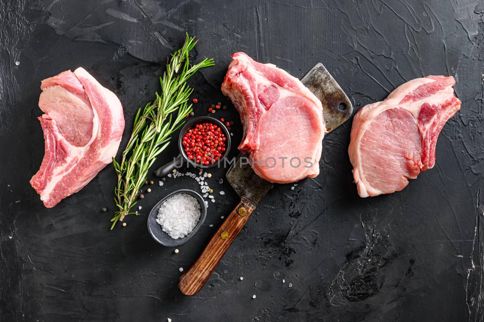 Organic Pork meat chop set over american classic butcher knife or cleaver with spices and rosemary and red pepper on black slate table top view. Space for text in corner