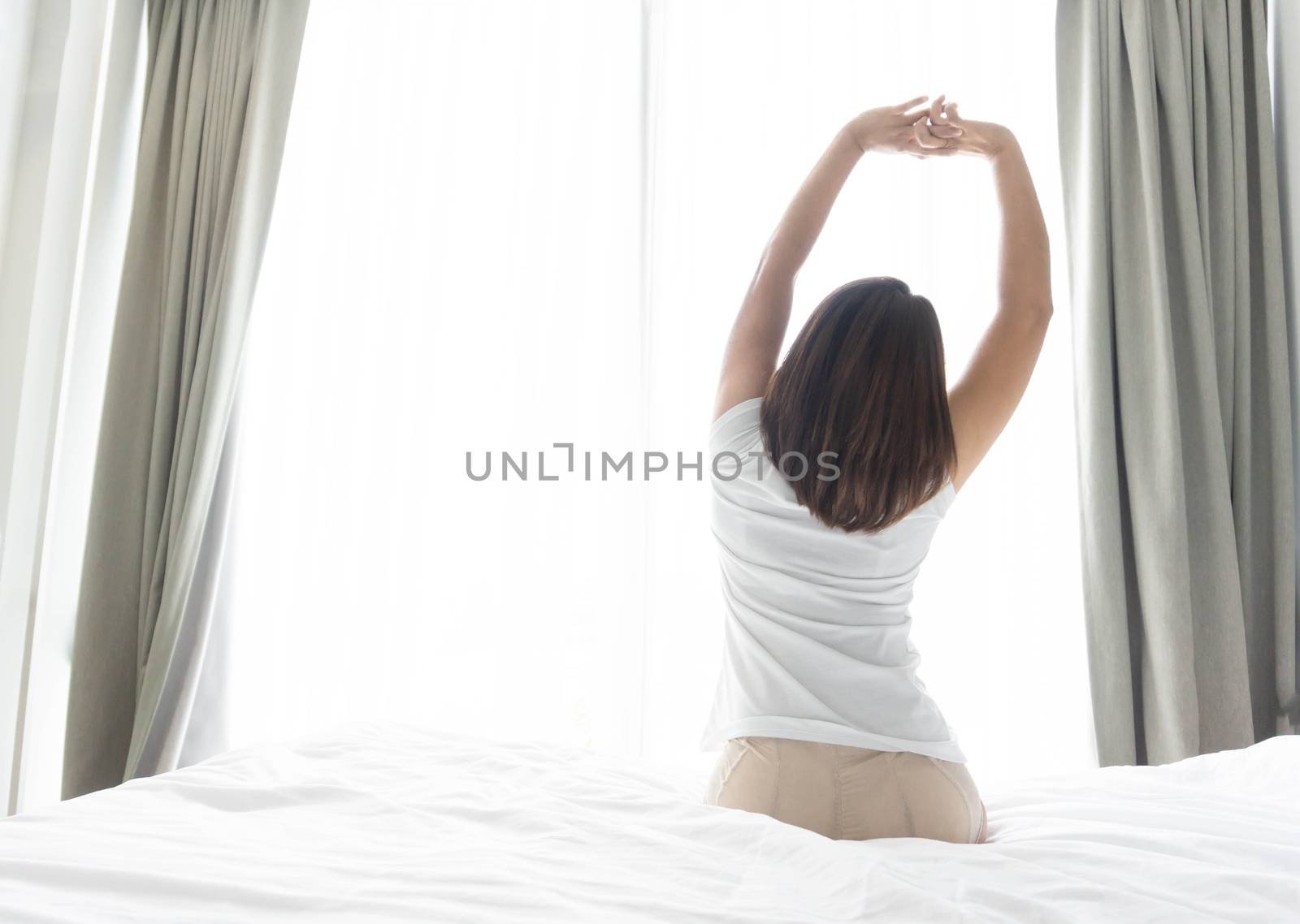 Close up woman sitting on the bed and stretching after waking up by pt.pongsak@gmail.com
