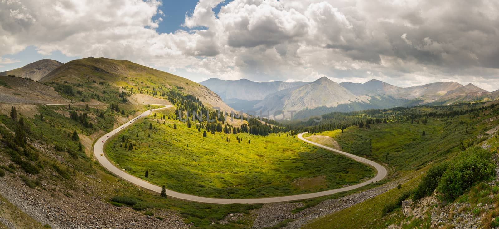 Panorama of wide curving bend on road climbing to top of Cottonwood Pass in Colorado as sports cars race to summit