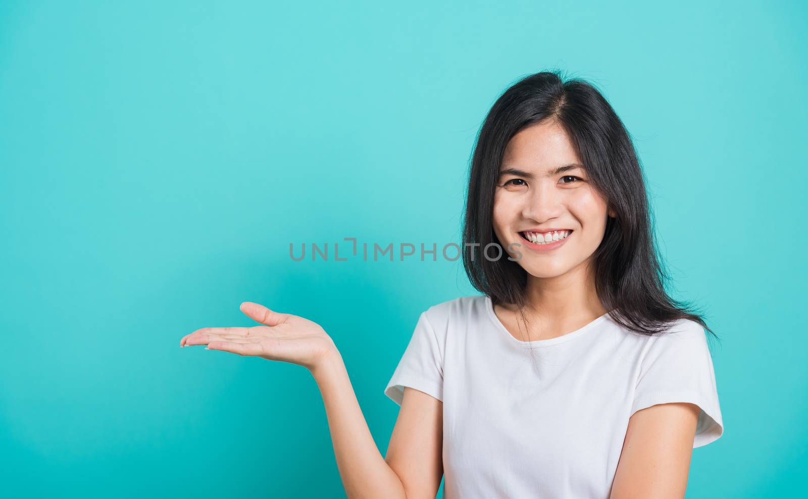 Portrait Asian beautiful young woman standing wear t-shirt, She showing hand to presenting product and looking at the camera, shoot photo in a studio on blue background, There was copy space