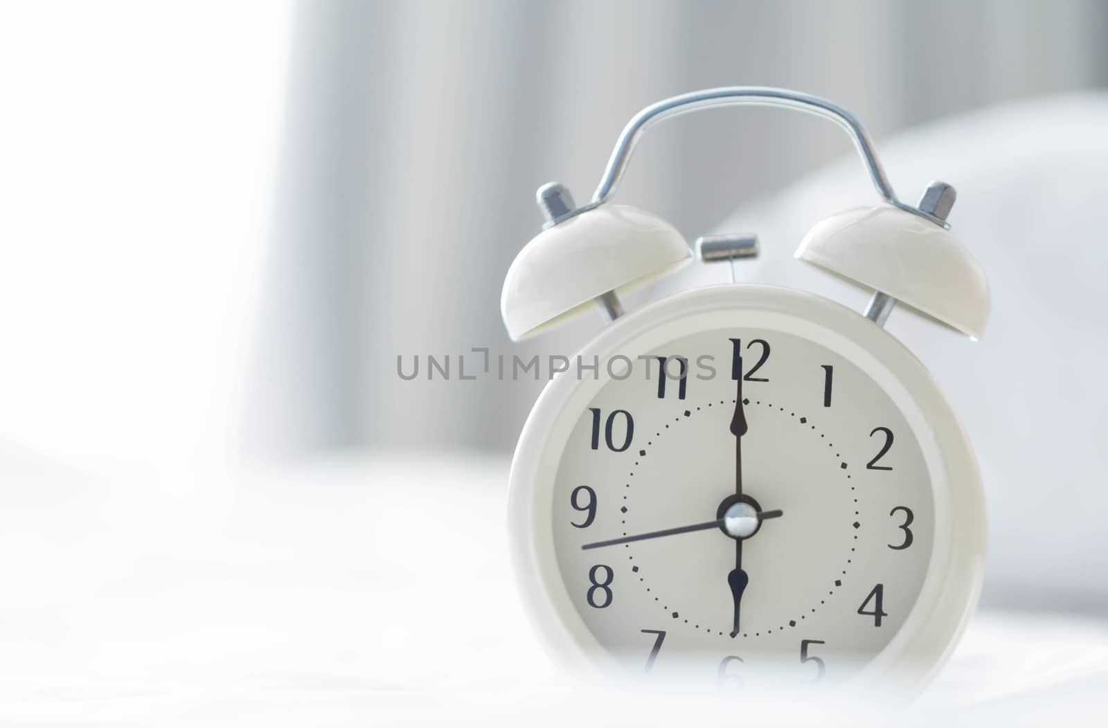 Alarm clock on white bad with light from window, selective focus