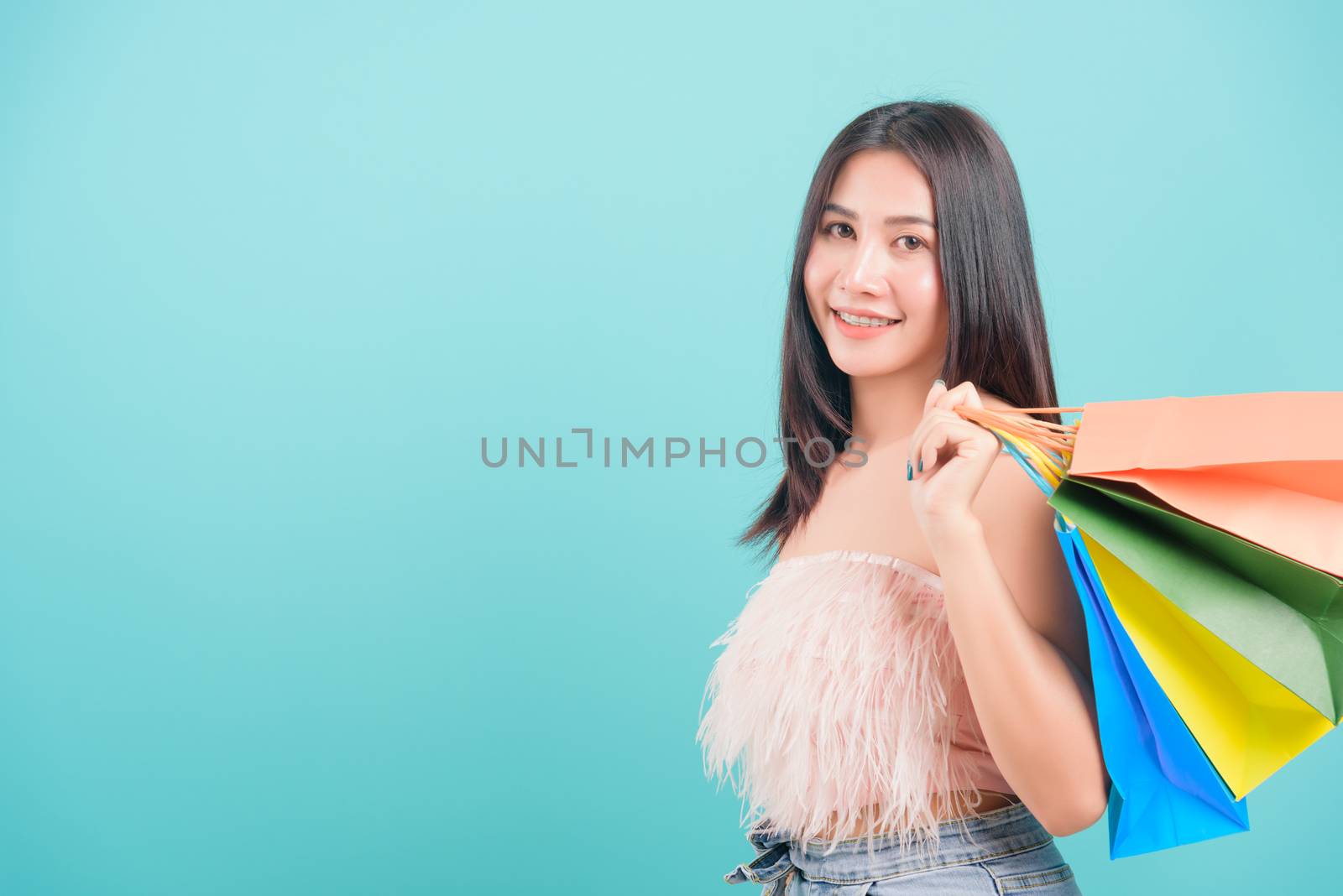 Asian happy portrait beautiful young woman standing smile in summer shopping her holding multicolor shopping bags on hand and looking to camera on blue background with copy space for text