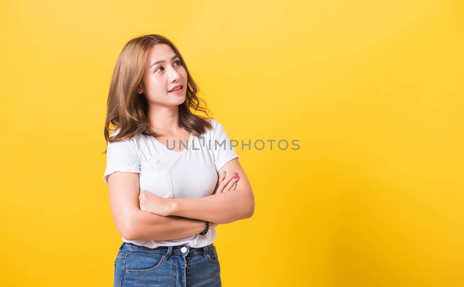 Asian Thai happy portrait beautiful cute young woman standing wear t-shirt her smile confidence with crossed arms looking to side up isolated, studio shot on yellow background and copy space