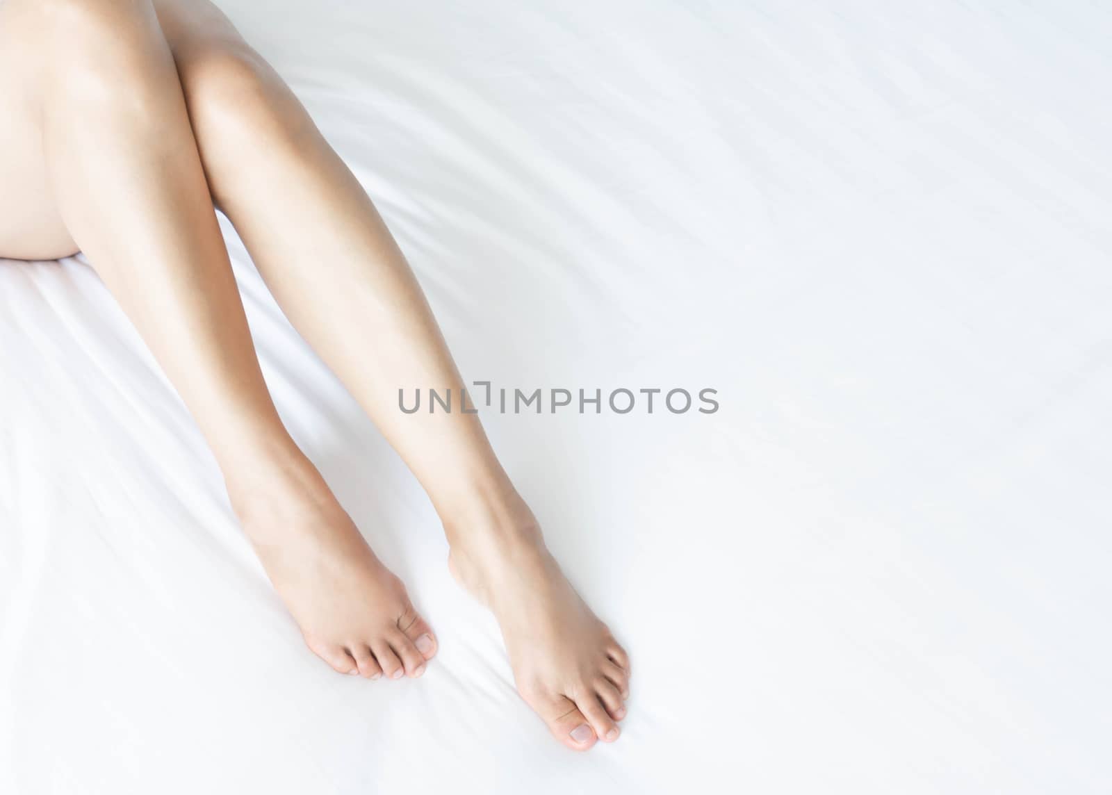 Closeup woman legs on white bed with over light form window, beauty and skin care concept, selective focus