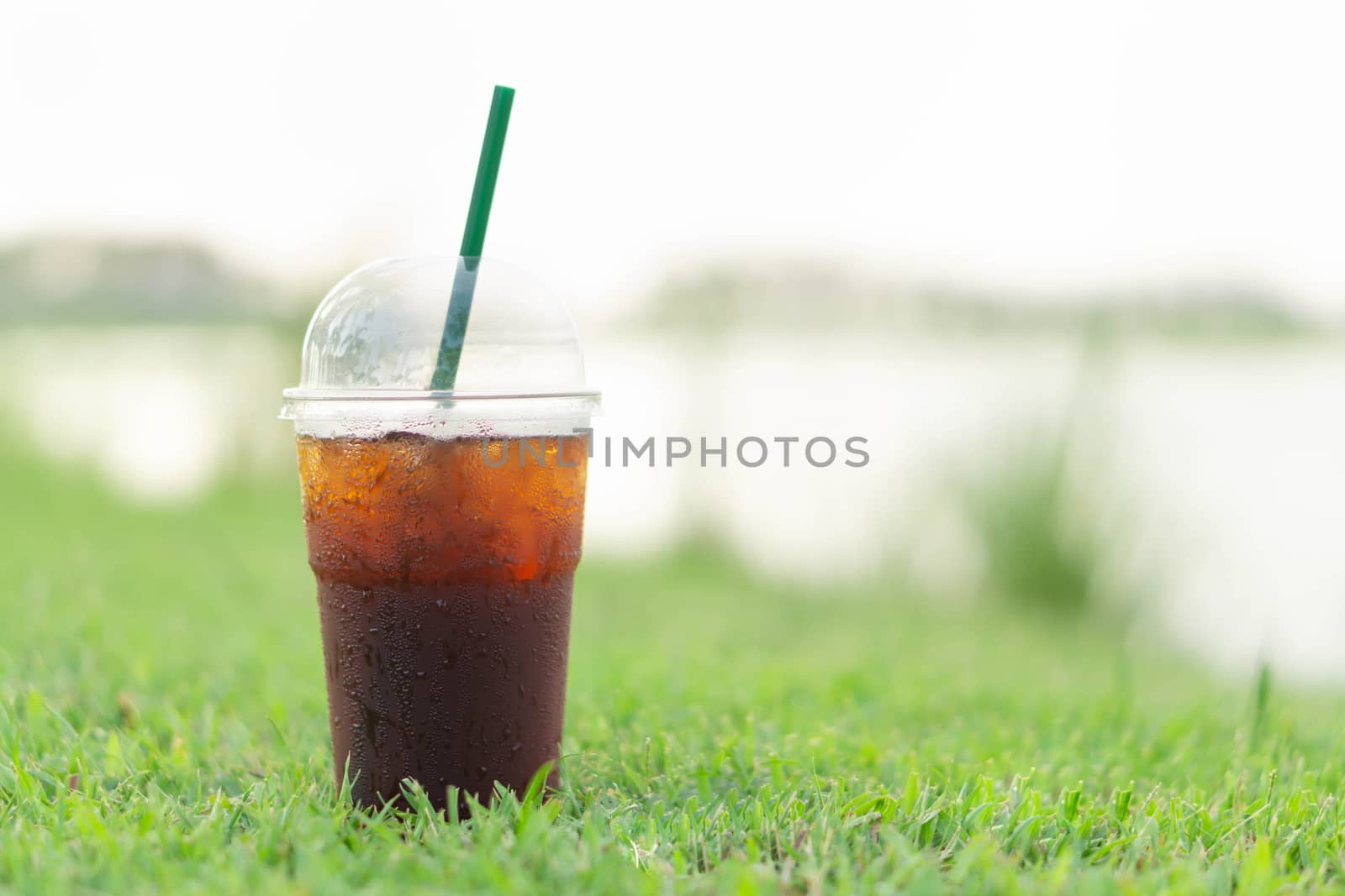 Close up glass of ice americano coffee with green grass nature background, selective focus