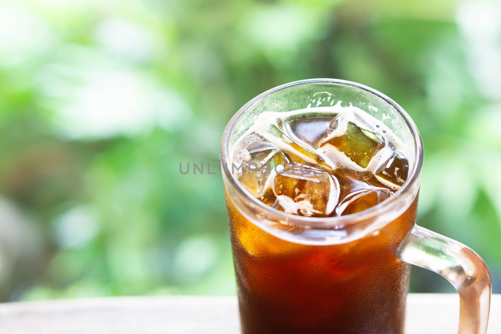 Closeup glass of ice americano coffee with green nature background, selective focus