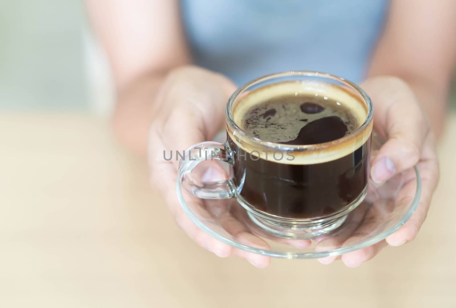 Closeup woman hand holding glass of hot americano coffee, selective focus, vintage tone