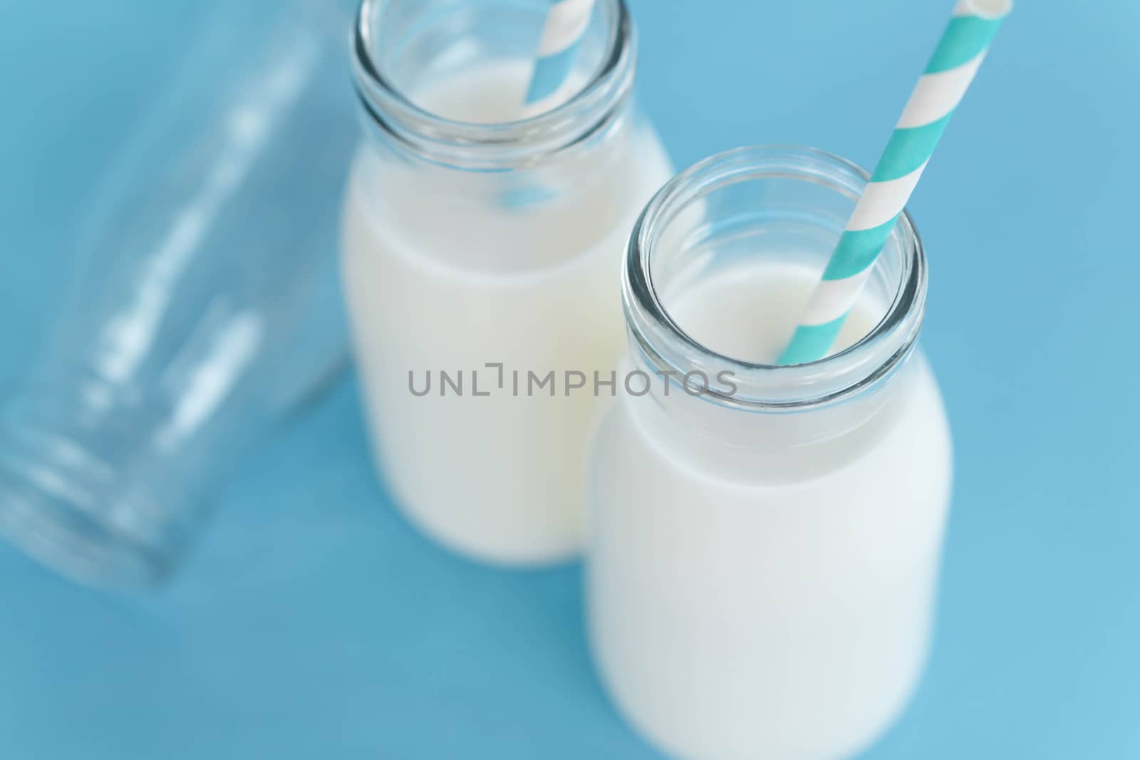 Close up topview bottle of fresh milk with straw on light blue background, selective focus