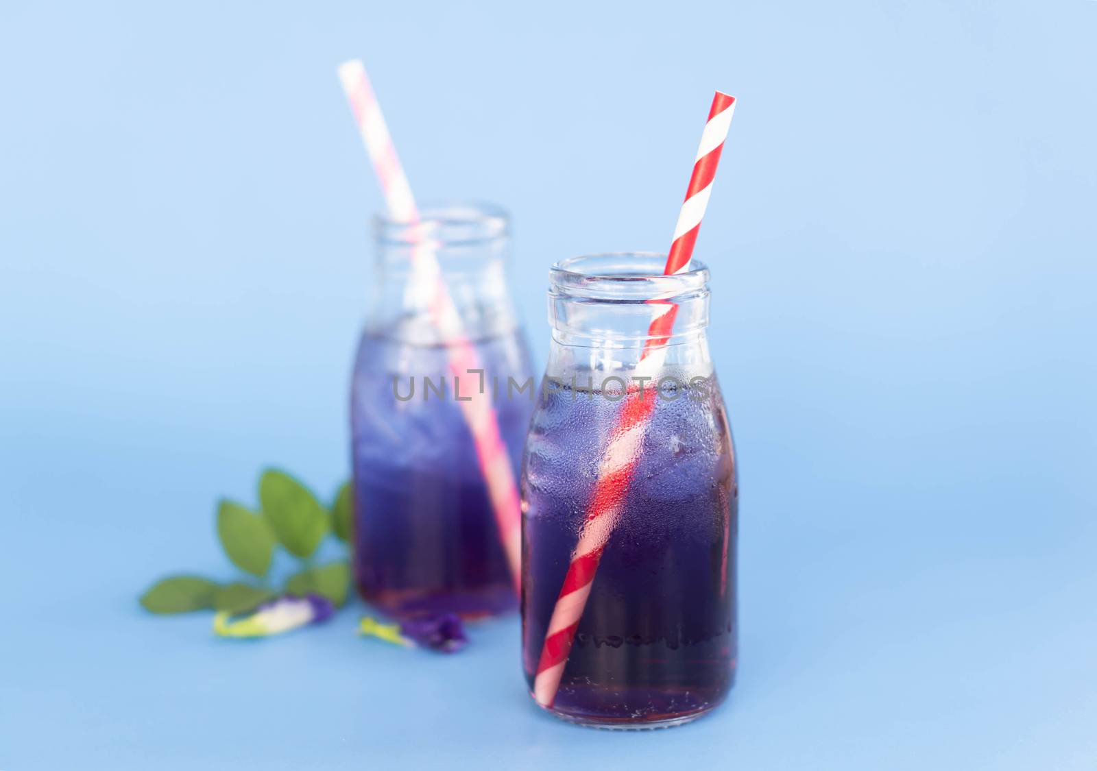 Butterfly pea juce in grass bottle with leaf and flower on light blue background, herb dink for healthy concept
