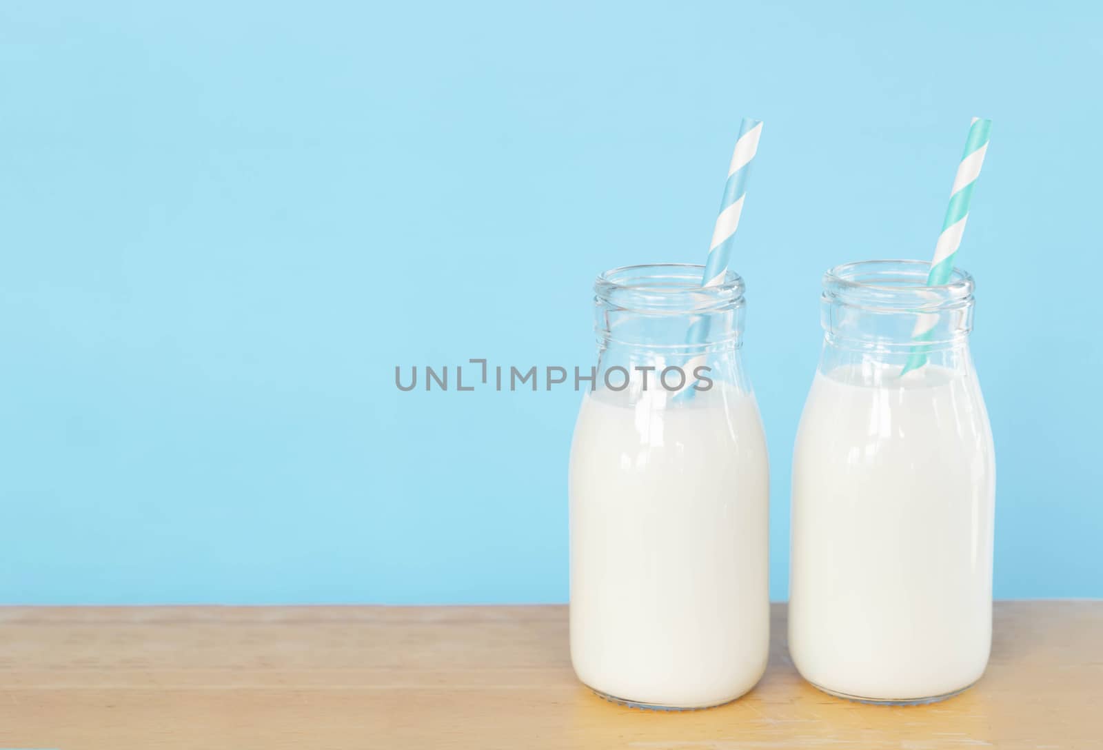 Bottle of fresh milk with straw on light blue background with copy space, food healthy concept