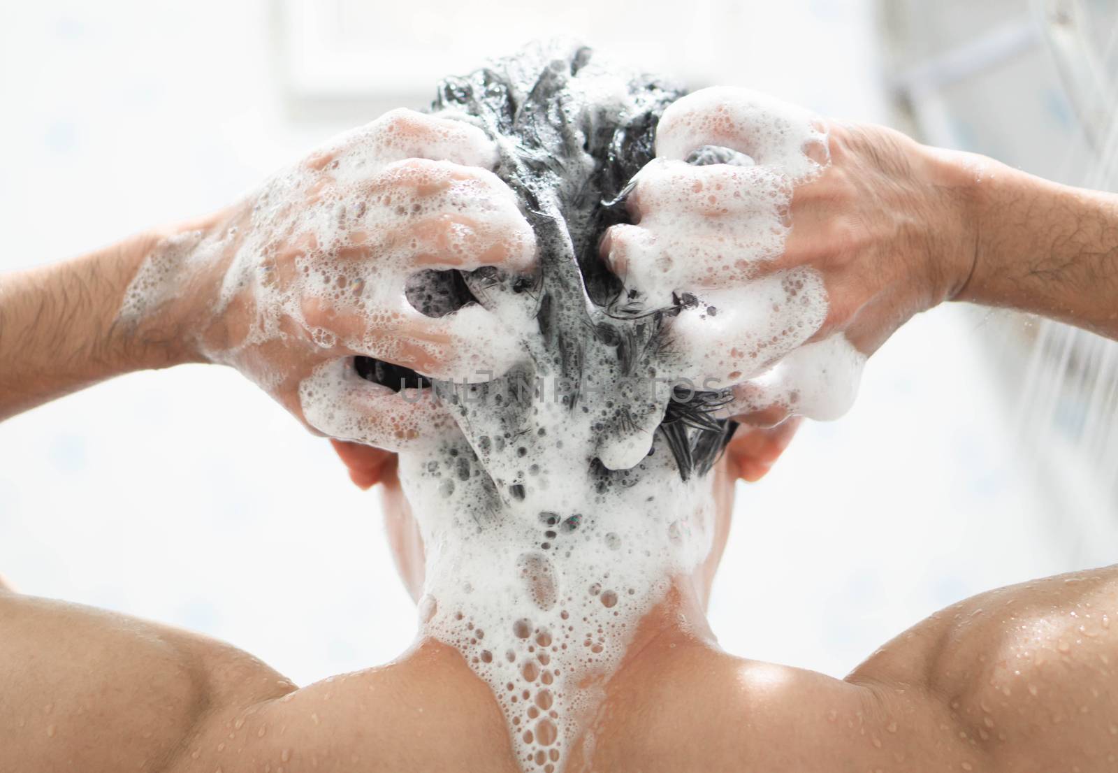 Closeup young man washing hair with with shampoo in the bathroom, health care concept, selective focus