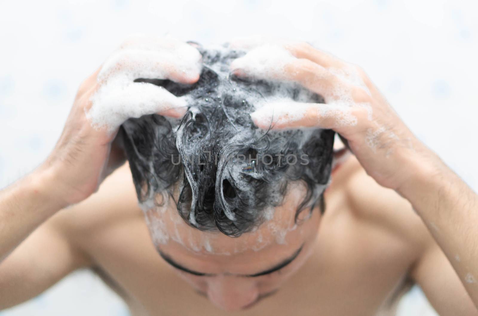 Closeup young man washing hair with with shampoo in the bathroom, health care concept, selective focus