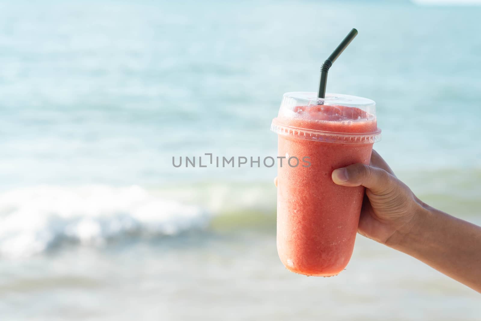 Hand holding glass of strawberry smoothie with sea water backgro by pt.pongsak@gmail.com