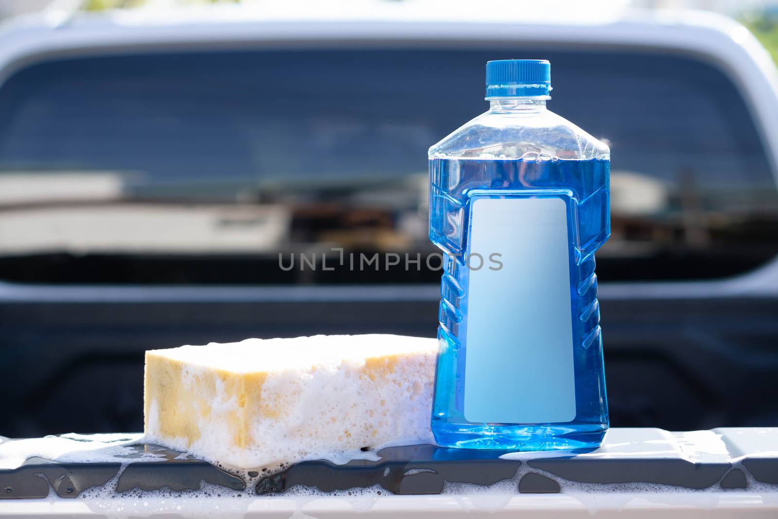 Close up bottle of car wash soap with yellow sponge for washing, selective focus