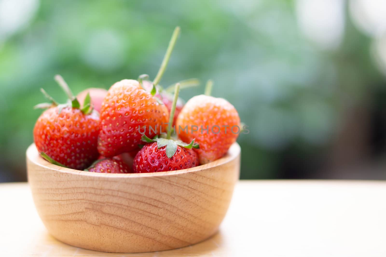 Closeup red strawberry in wood bowl with green nature background, selective focus