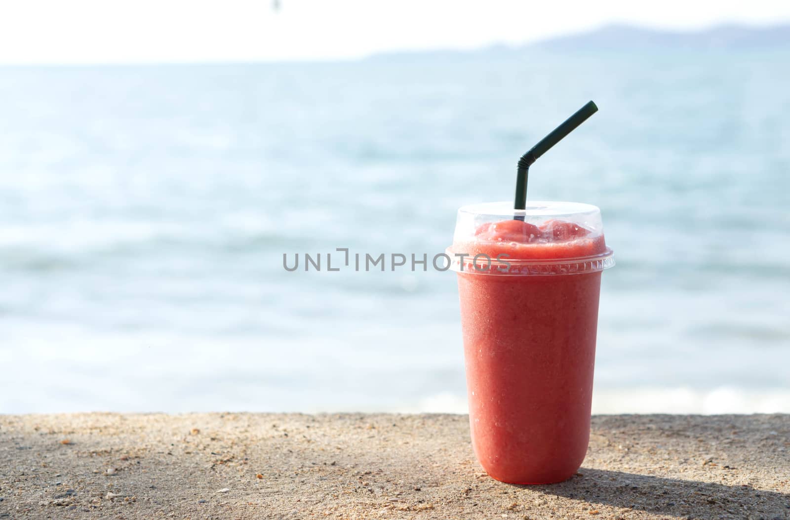 Closeup glass of strawberry smoothie with lignt in the morning and sea water background, Holiday and relax time