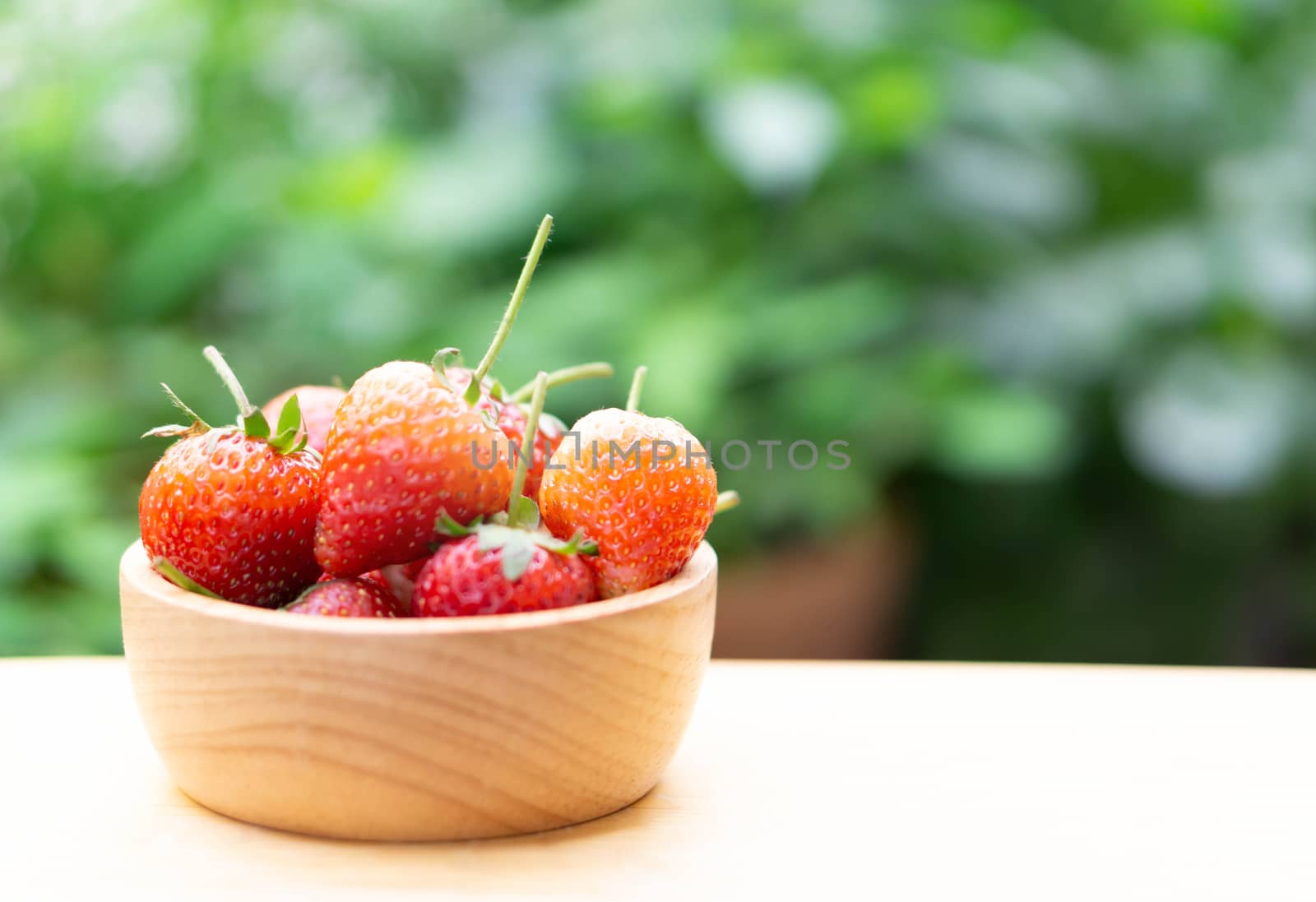 Closeup red strawberry in wood bowl with green nature background, selective focus