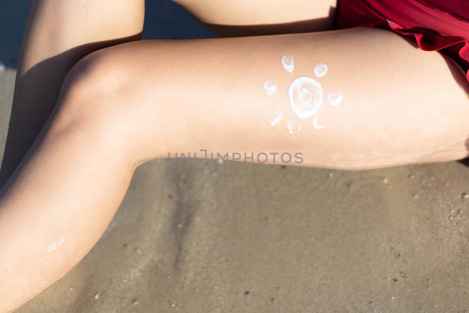 Closeup woman applying sun screen lotion on her legs with draw sun symbol on the beach, Holiday and relax concept