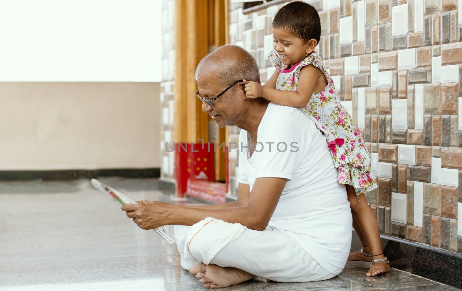 Little Granddaughter playing with grandfather by pulling grandpa's ears at home - concept of togetherness, fun, happiness and kids relationship with grandparents