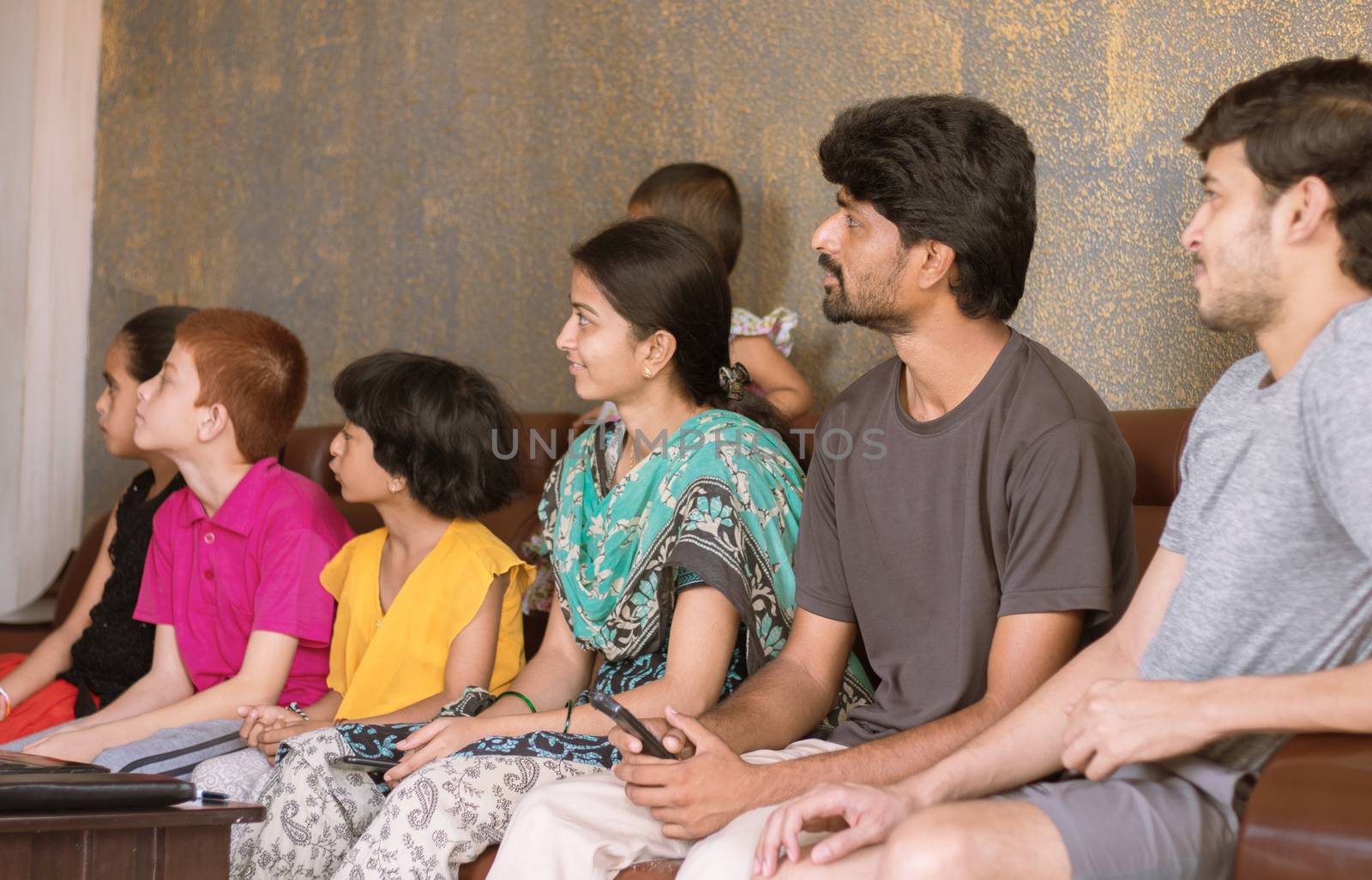 Group of family Siblings watching tv on sofa at home - concept of family bonding, togetherness, weekend entertainment and socializing.