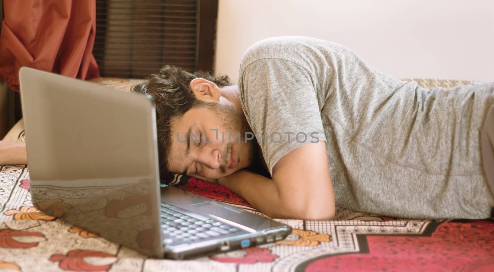 Tired young man sleeping in bed with laptop - hard work, laziness of working from home or WFH during coronavirus or covid-19 lock down concept