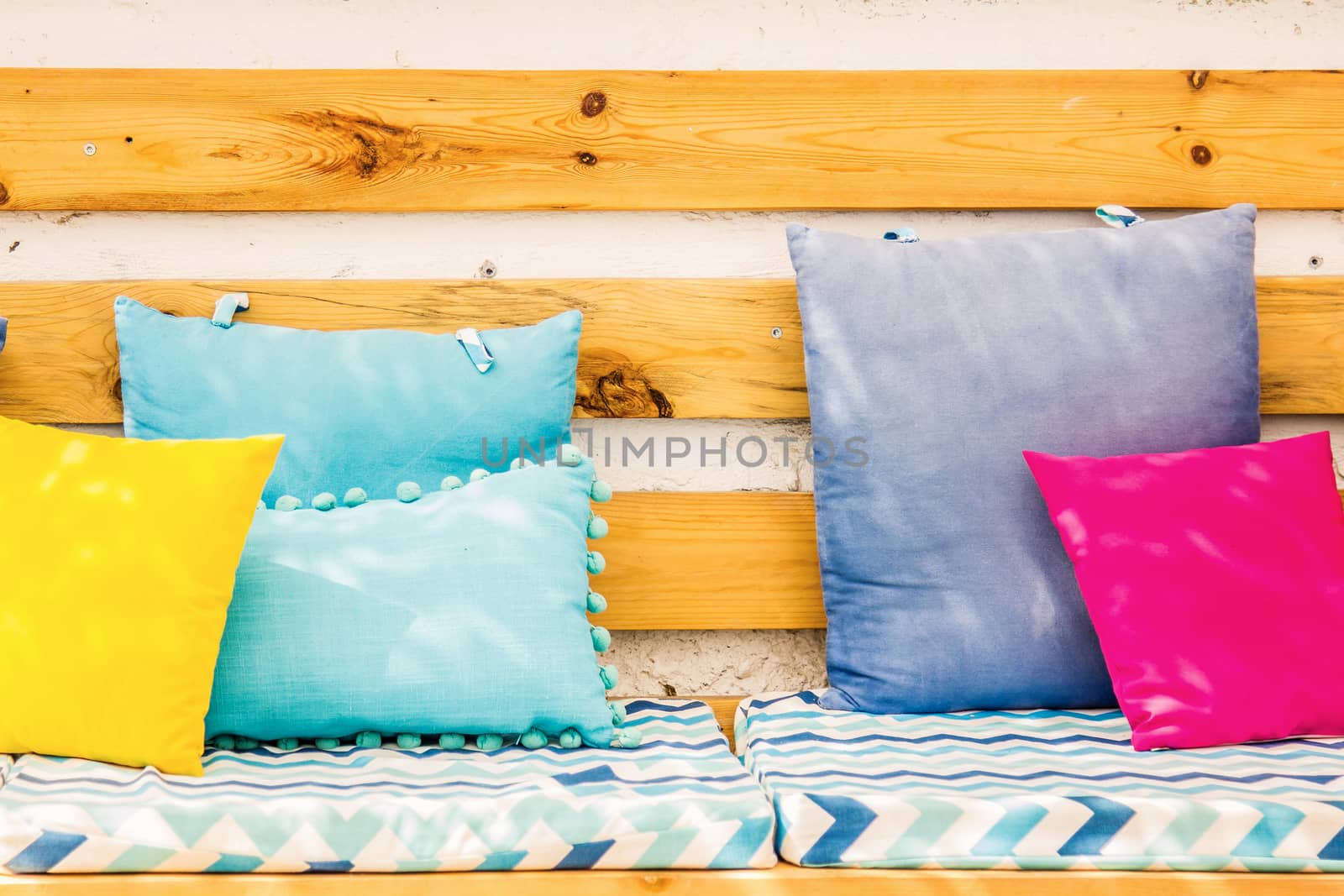 Close up pillows on an outdoor patio chair, with a blue striped cushioned bench by tussik