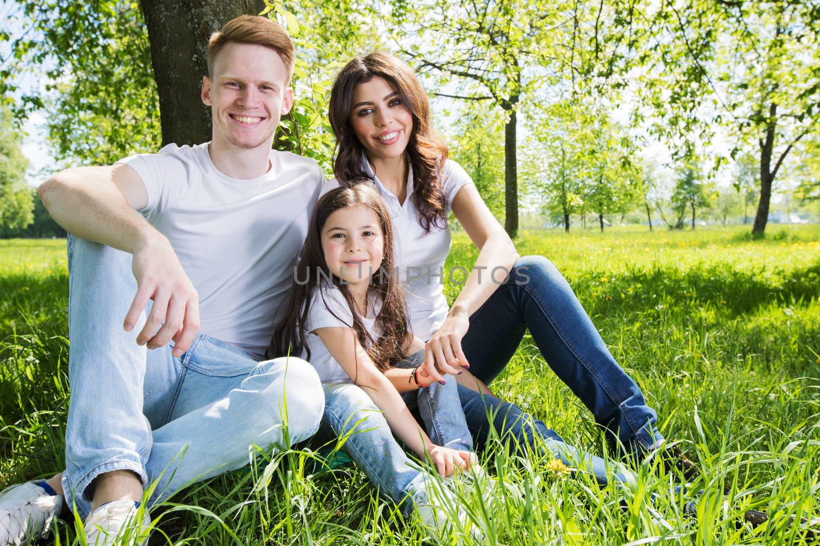 Family of three sitting on spring park meadow grass being happy