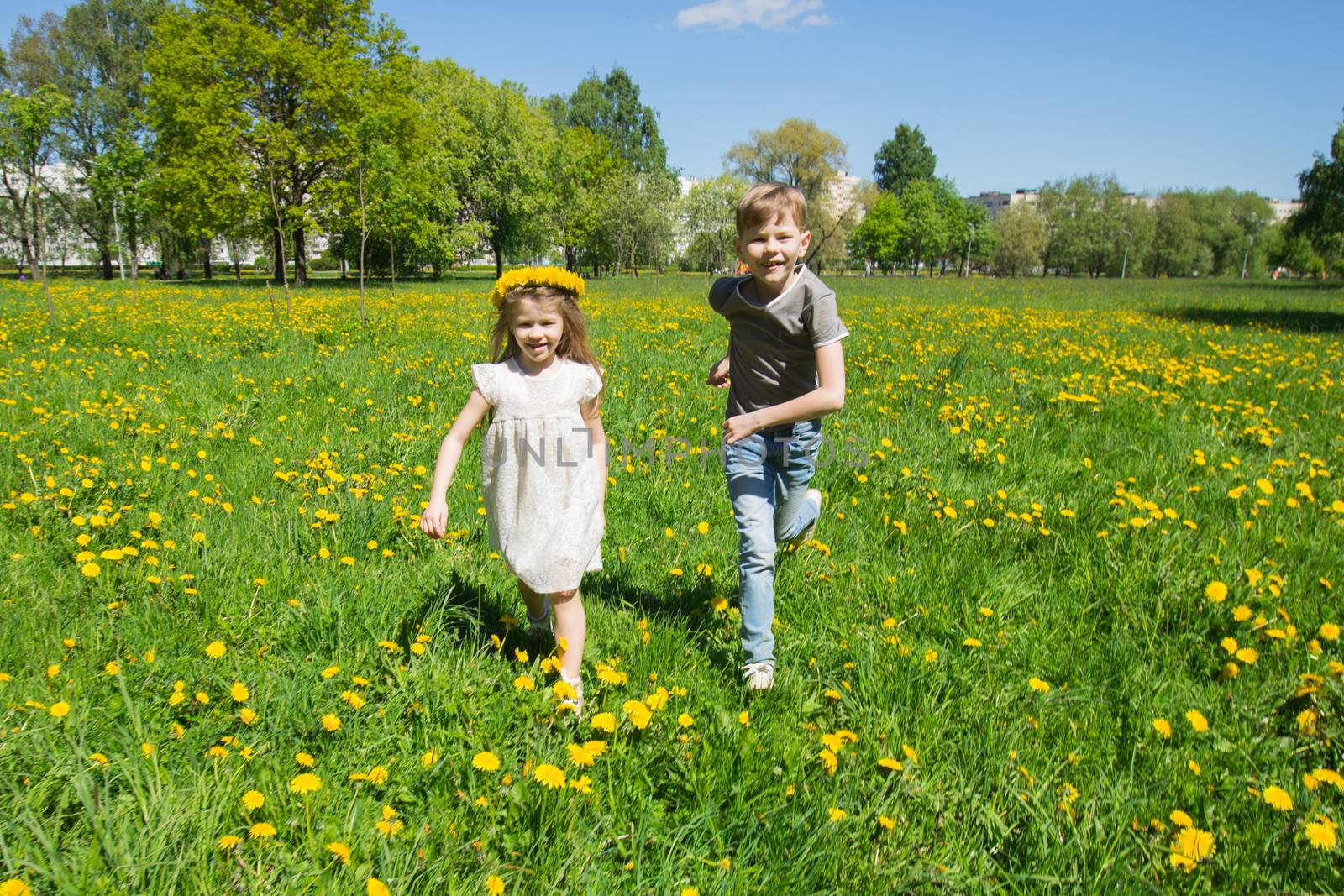 Young boy and girl brither and sister running in a sunny meadow with dandelion flowers family fun concept