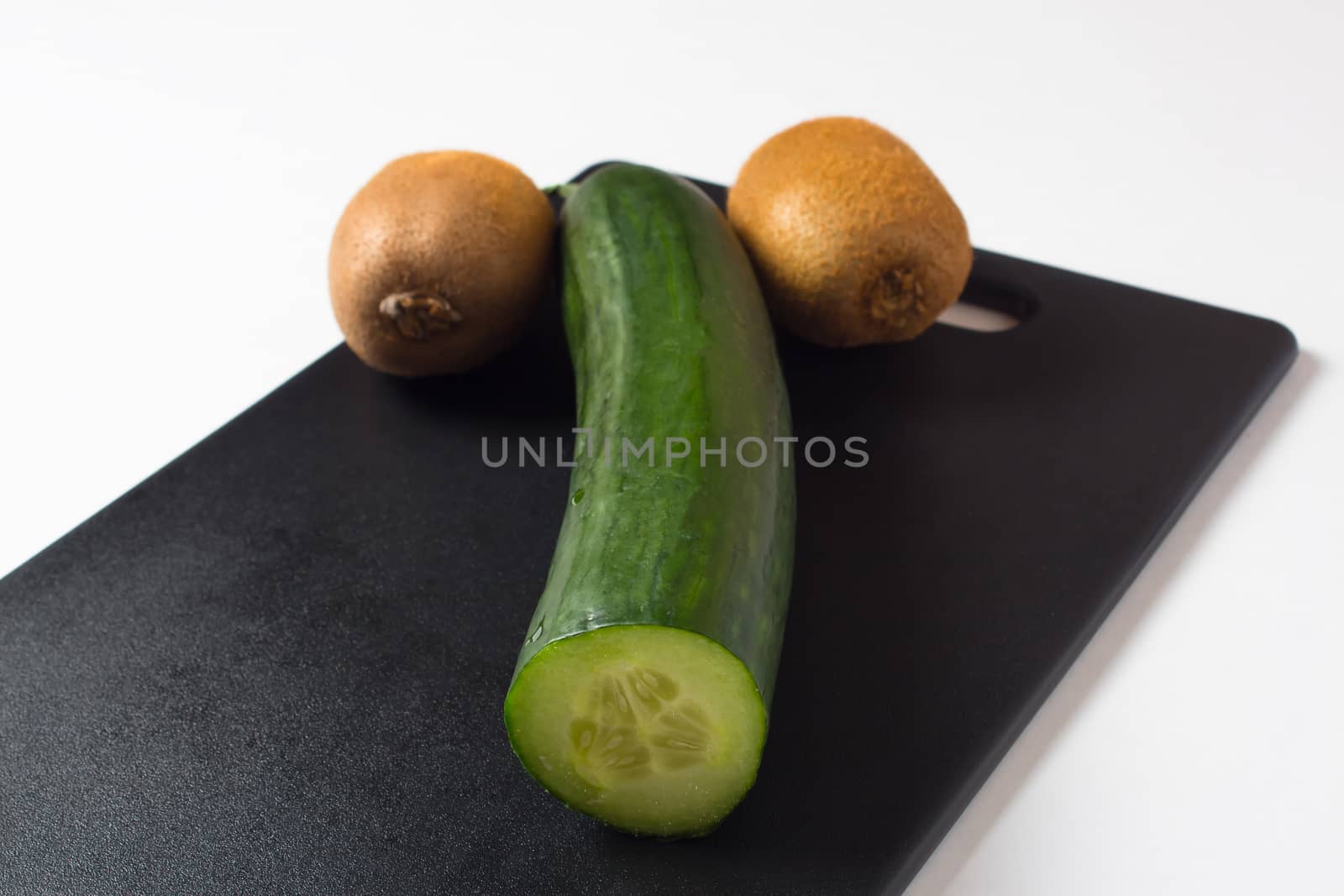 A cucumber and two kiwis lie on a black cutting Board. Diet food and salads for a healthy lifestyle. The likeness of a phallic symbol or masculine dignity. Fresh vegetables and fruits.