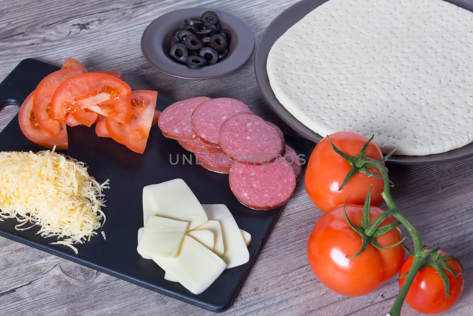 Pizza base and ingredients for its preparation. Tomatoes, sausage, cheese and olives are on the kitchen table. Cooking pizza at home.