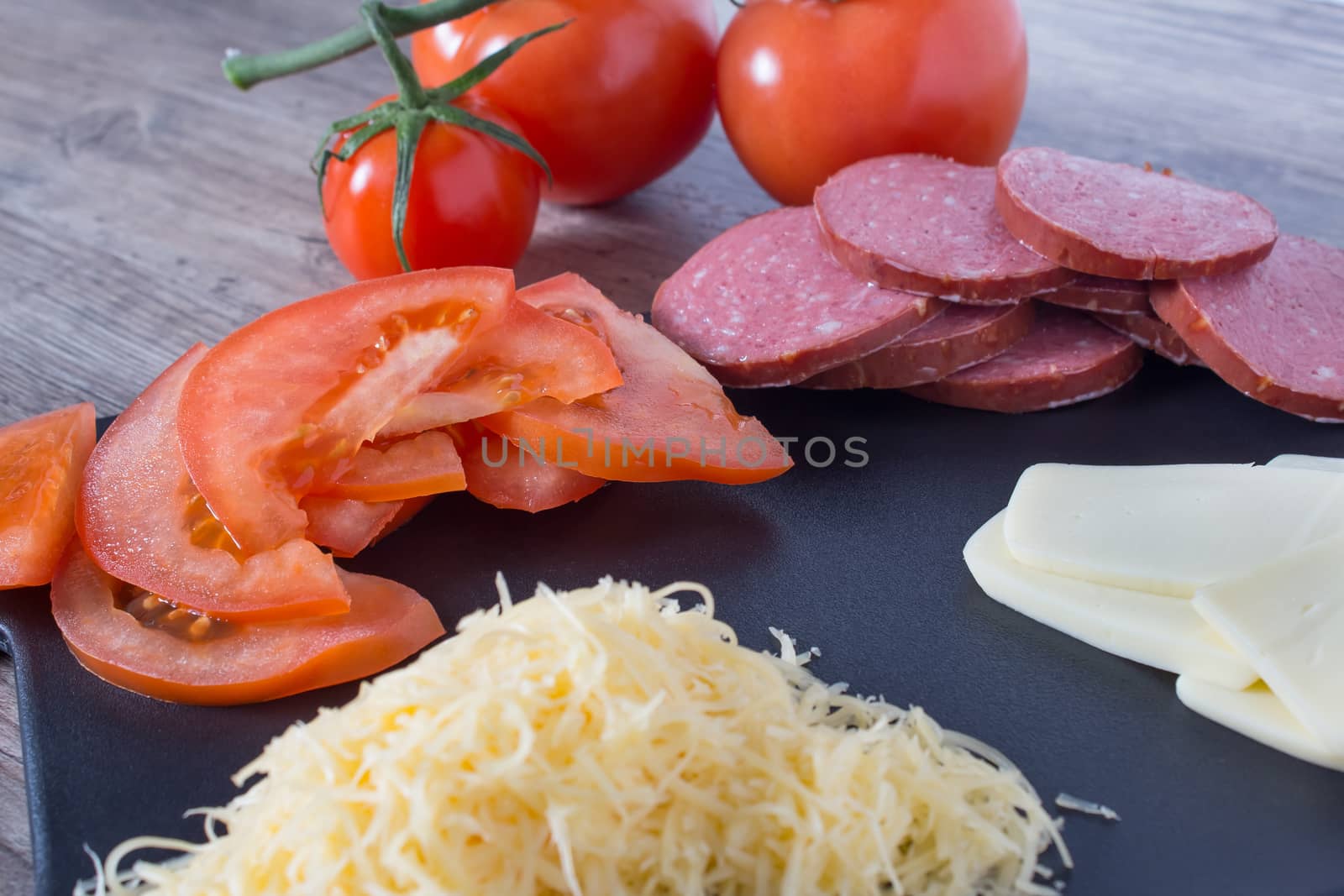 Sliced tomatoes, sausage and cheese are on the cutting Board on the kitchen table. We cook at home