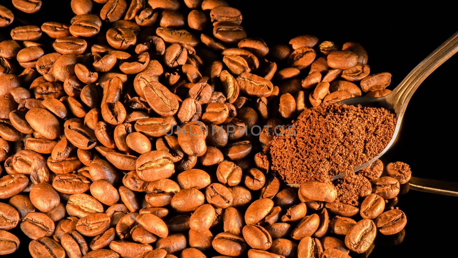 Coffee beans close-up with a spoon of ground coffee on a mirror background.