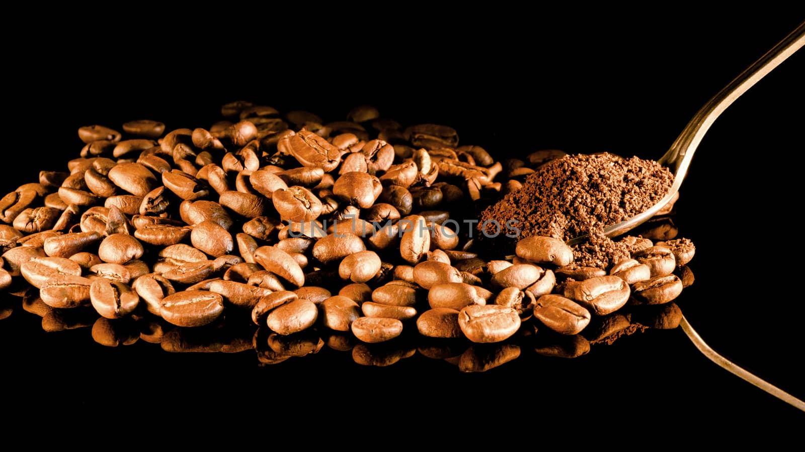 Coffee beans close-up with a spoon of ground coffee on a mirror background.