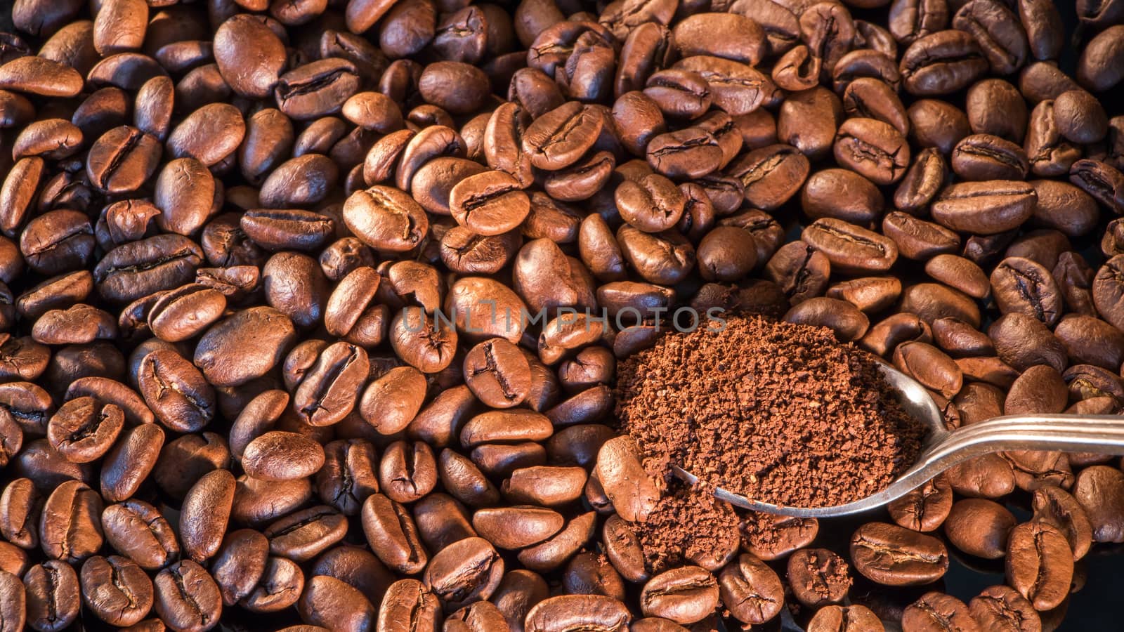 Coffee beans close-up with a spoon of ground coffee on a mirror background.