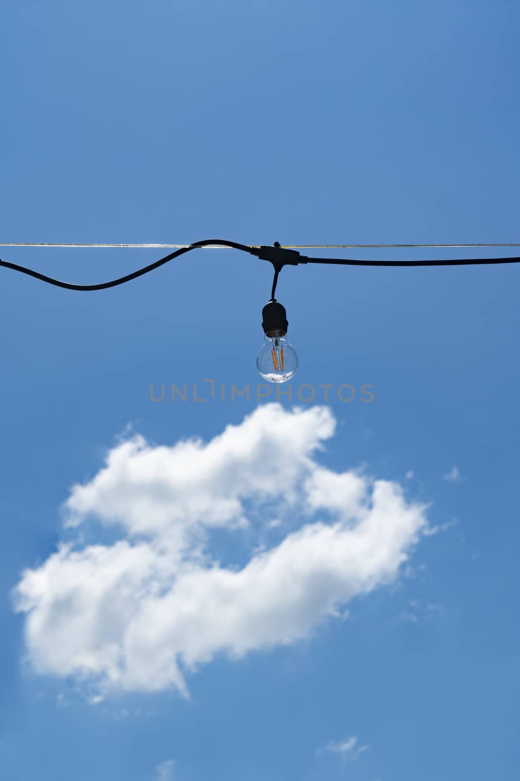 a light bulb hanging outdoors with the blue sky with a white cloud in the background