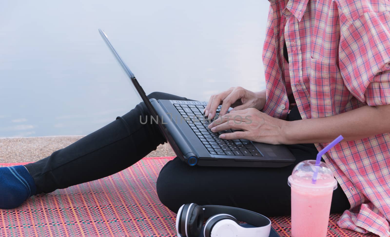 A woman using laptop computer while sitting beside river.