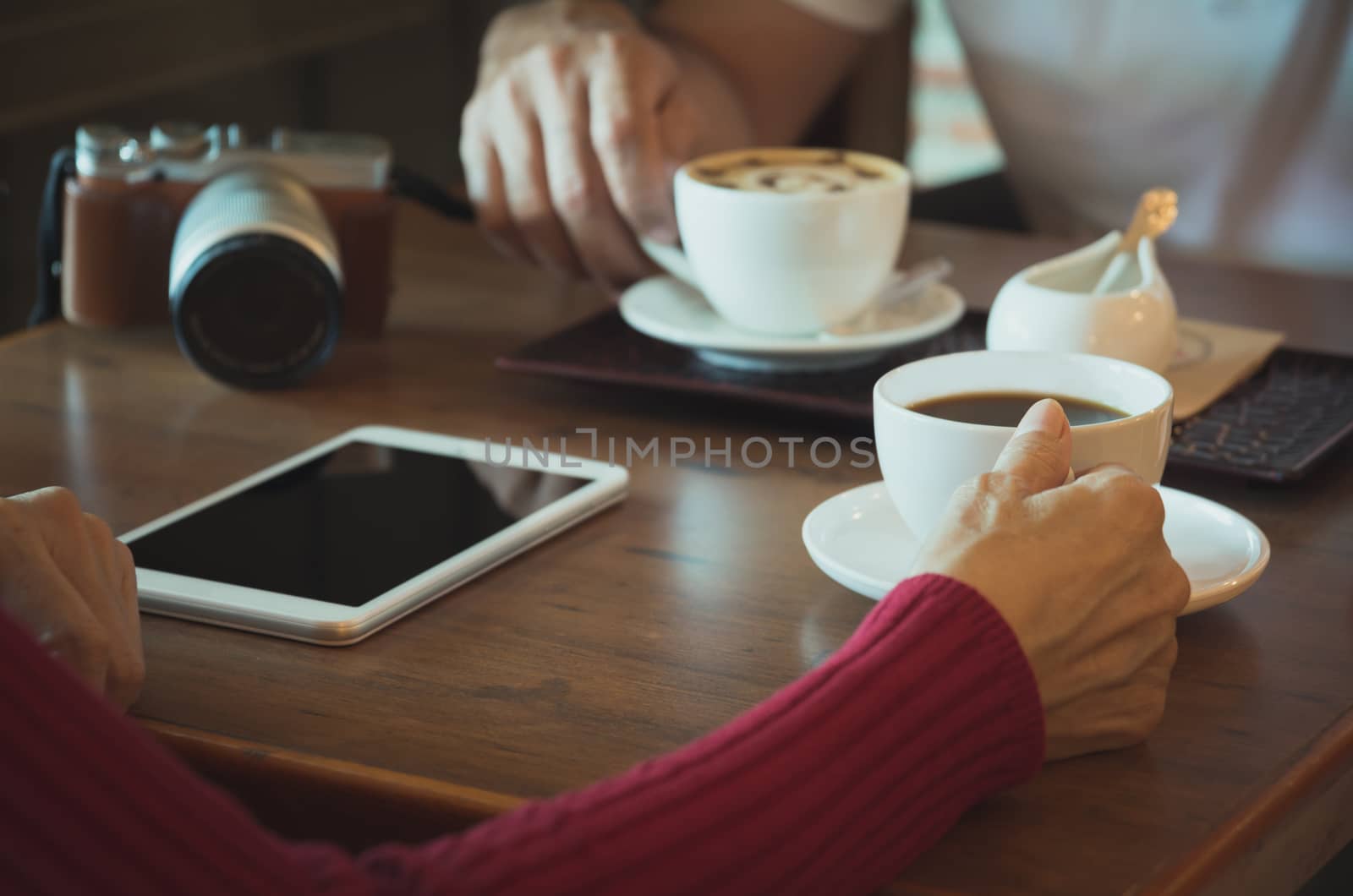 Female with tablet and camera coffee cup on wooden table.