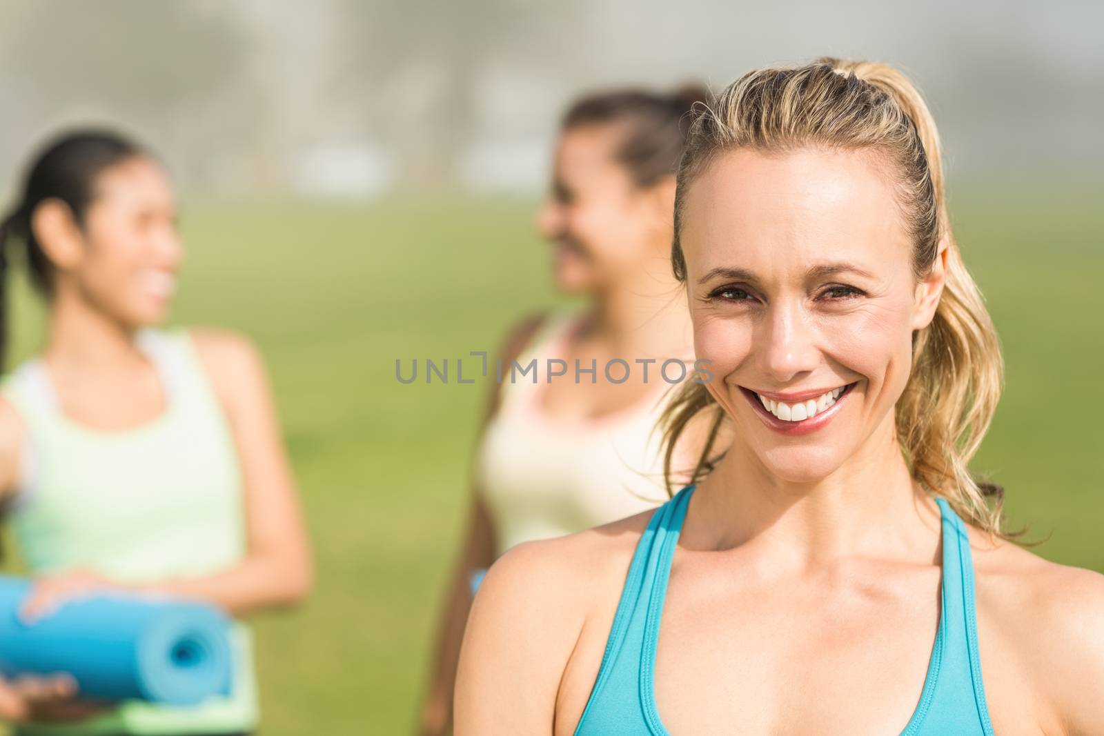 Portrait of smiling sporty blonde in front of friends in parkland