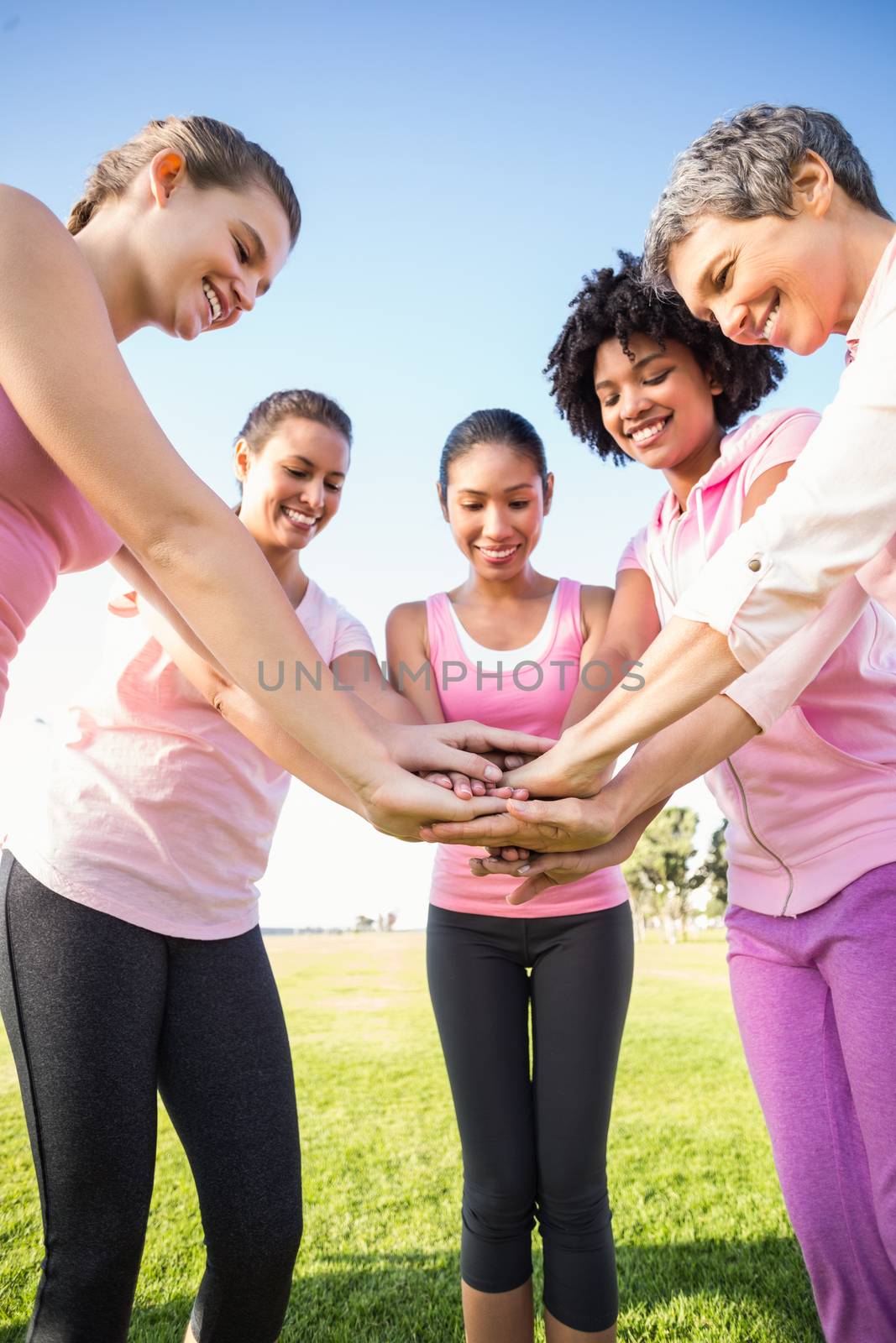 Women wearing pink for breast cancer and putting hands together by Wavebreakmedia